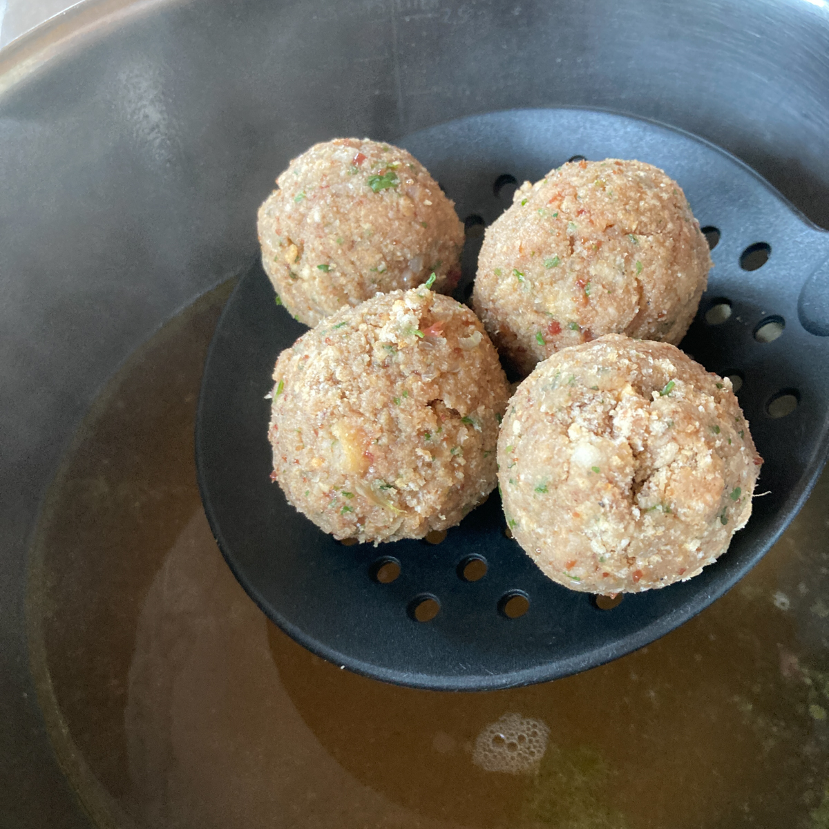 Vier Leberknödel auf Schaumkelle, die gerade in die Suppe gelegt werden.