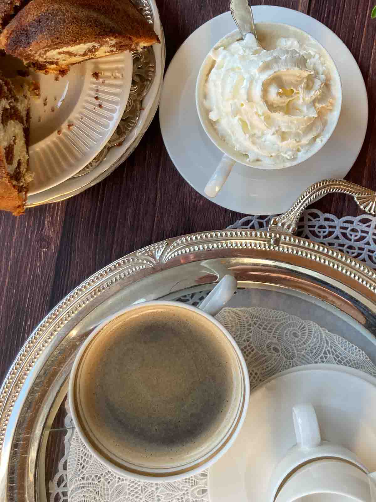 Rundes Silbernes Tablett mit Kaffeetasse, Gugelhupf auf Teller, Kaffeetasse mit Schlagobers.