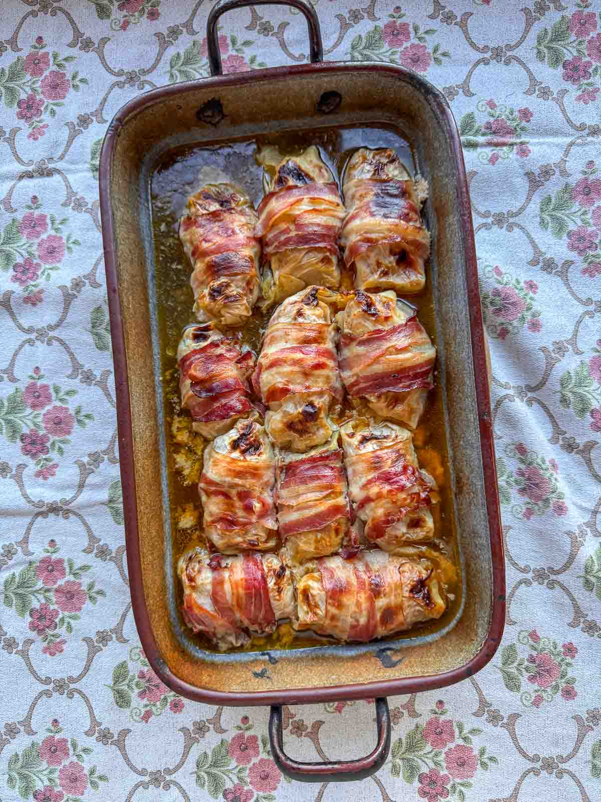 Krautrouladen in Bräter auf Blumentischtuch.