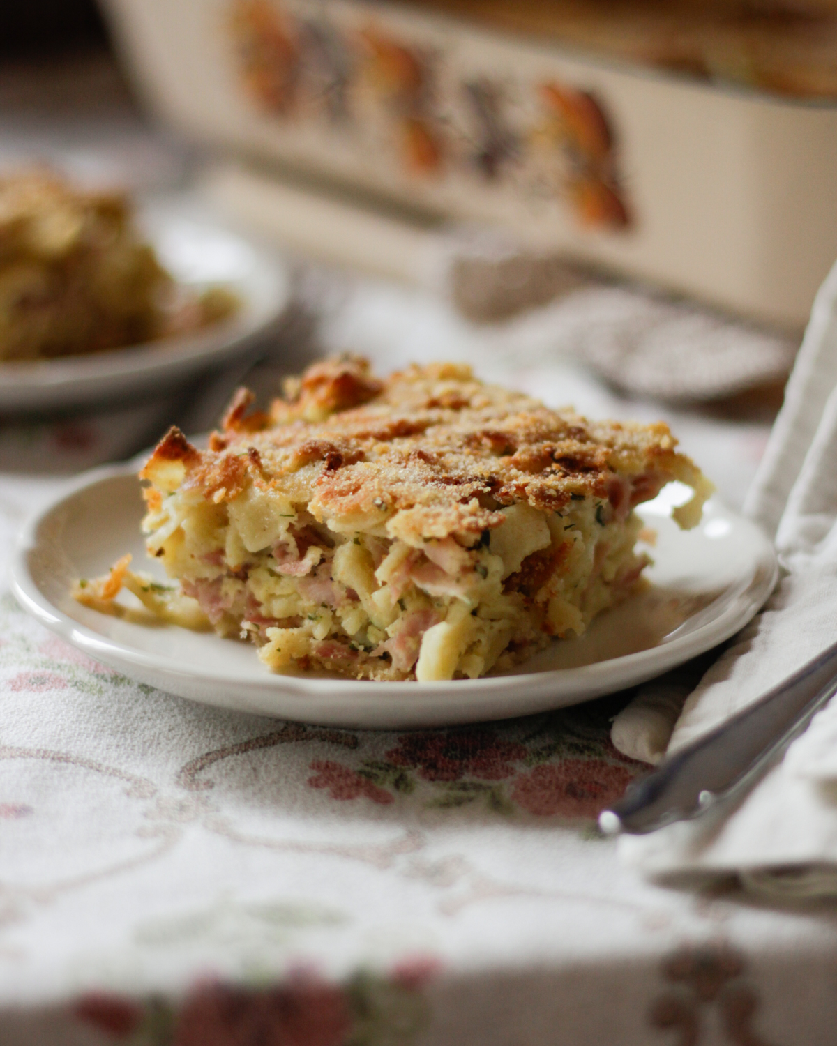 Teller mit Schinkenfleckerl auf geblümtem Tischtuch - Austrian Schinkenfleckerl recipe.