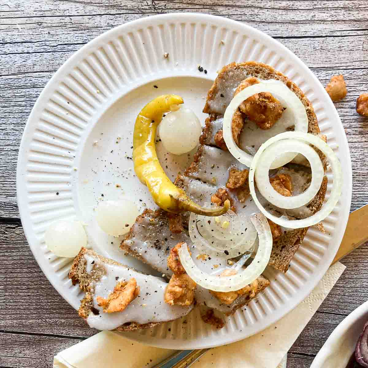 Grammelschmalzbrot mit Zwiebelringen, eingelegter Pfefferoni und bestreut mit Grammeln