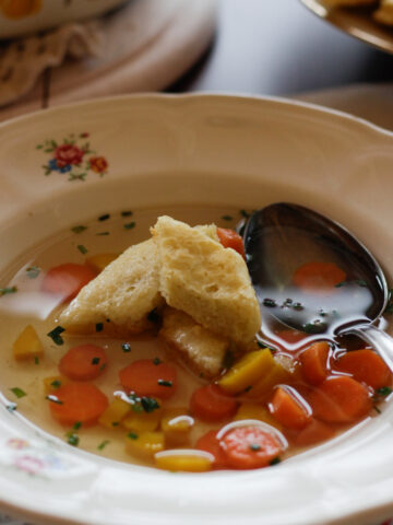 Rautenförmige Biskuitschöberl auf einem blumenverzierten Teller mit Gemüsesuppe.