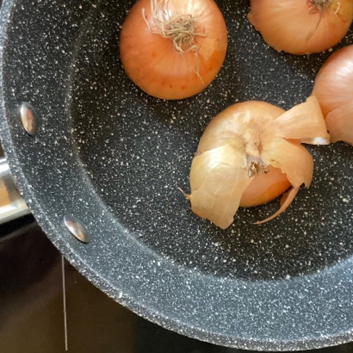 Vier Zwiebelhälften mit Schale in beschichteter Pfanne.