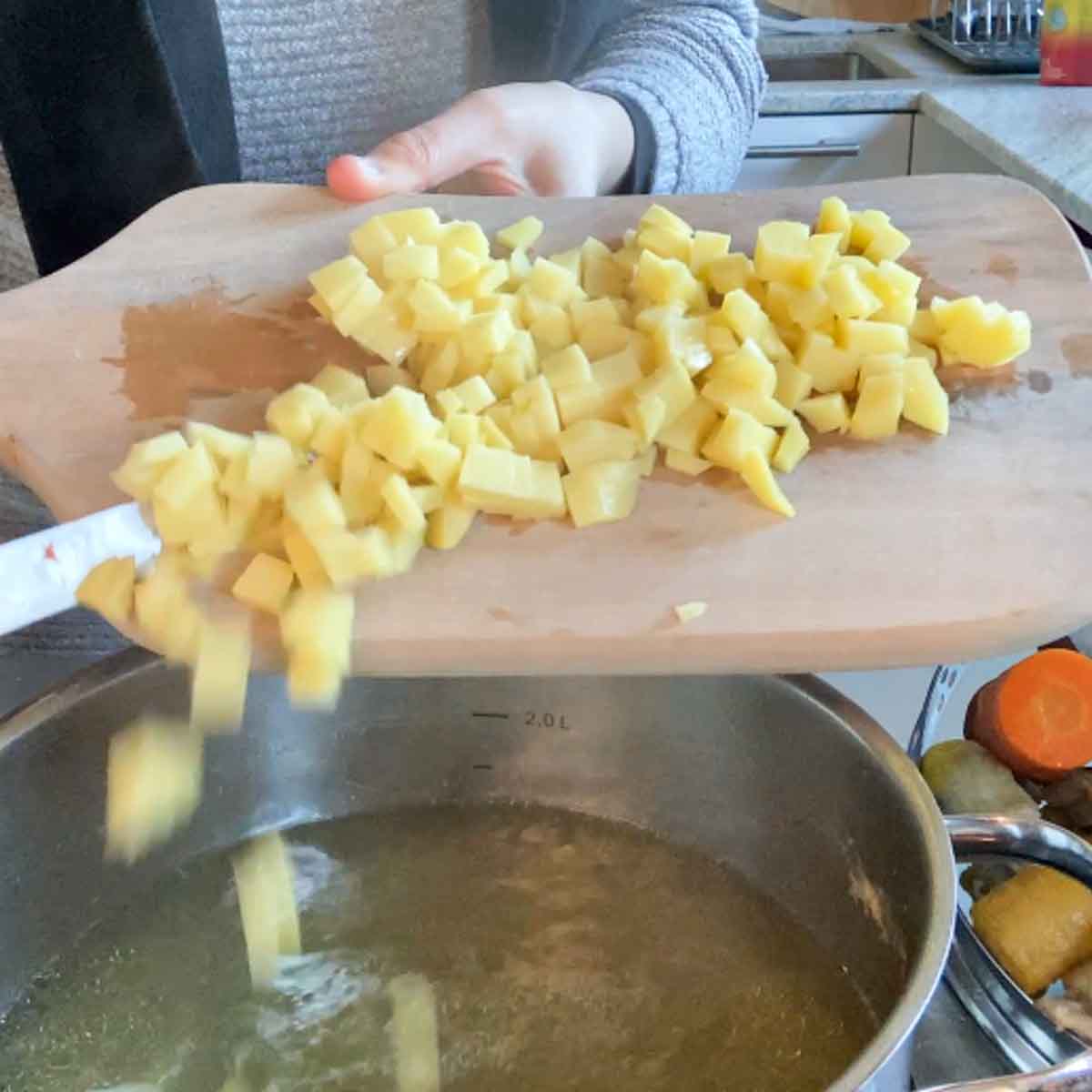 Klein geschnittene Kartoffelstücke, die in Topf geleert werden.