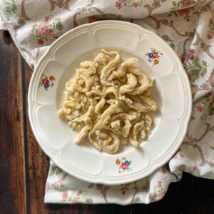 Spätzle ohne Sauce auf rustikalem Blumenteller, im ntergrund Blumentischtuch und Holzoberfläche. - Homemade Spaetzle Recipe.