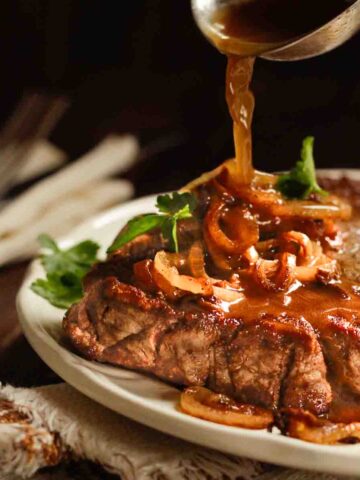 Zwiebelrostbaten auf Holztisch mit rustikaler Stoffserviette, mit Zwiebelsauce übergossen. - Braised Roast Beef on white plate poured with onion sauce.