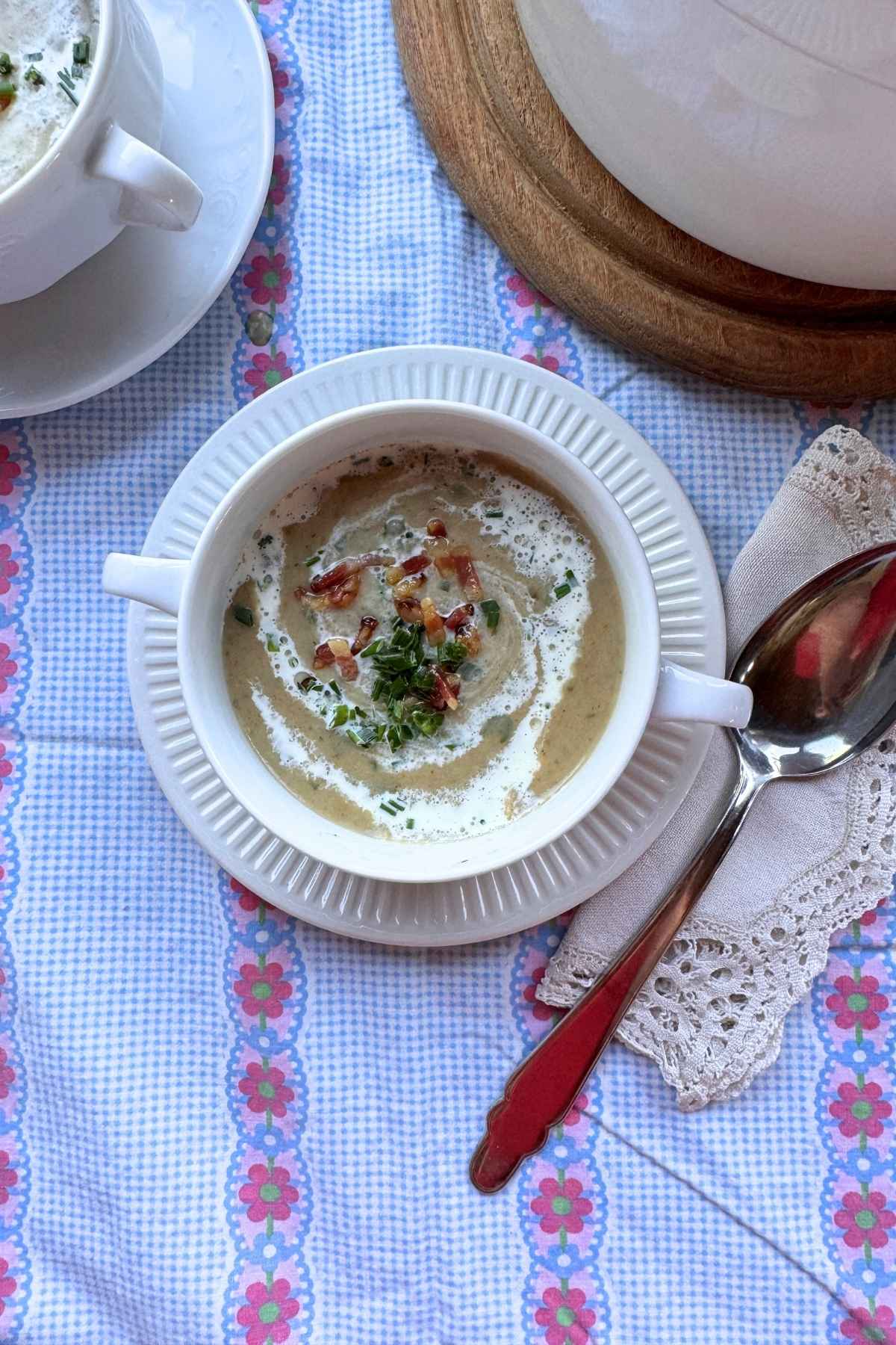 Brotsuppe in weißer Henkelschüssel auf geblümtem Tischtuch.