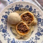 Knödel aus Mehlteig auf blaum geblümtem nostalgischem Teller angerichtet.