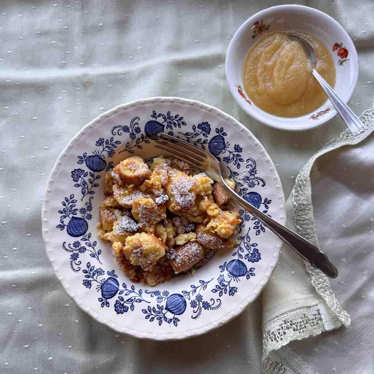 Semmelschmarrn auf blau geblümtem Teller, Apfelmus in kleiner Schüssel.